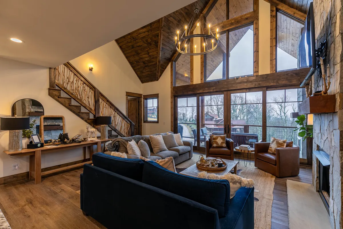 An interior space featuring large windows that frame scenic outdoor views, with a central seating arrangement and a chandelier overhead. The inviting setting suggests a perfect spot to relax and soak in the natural surroundings after a day of outdoor activities.
