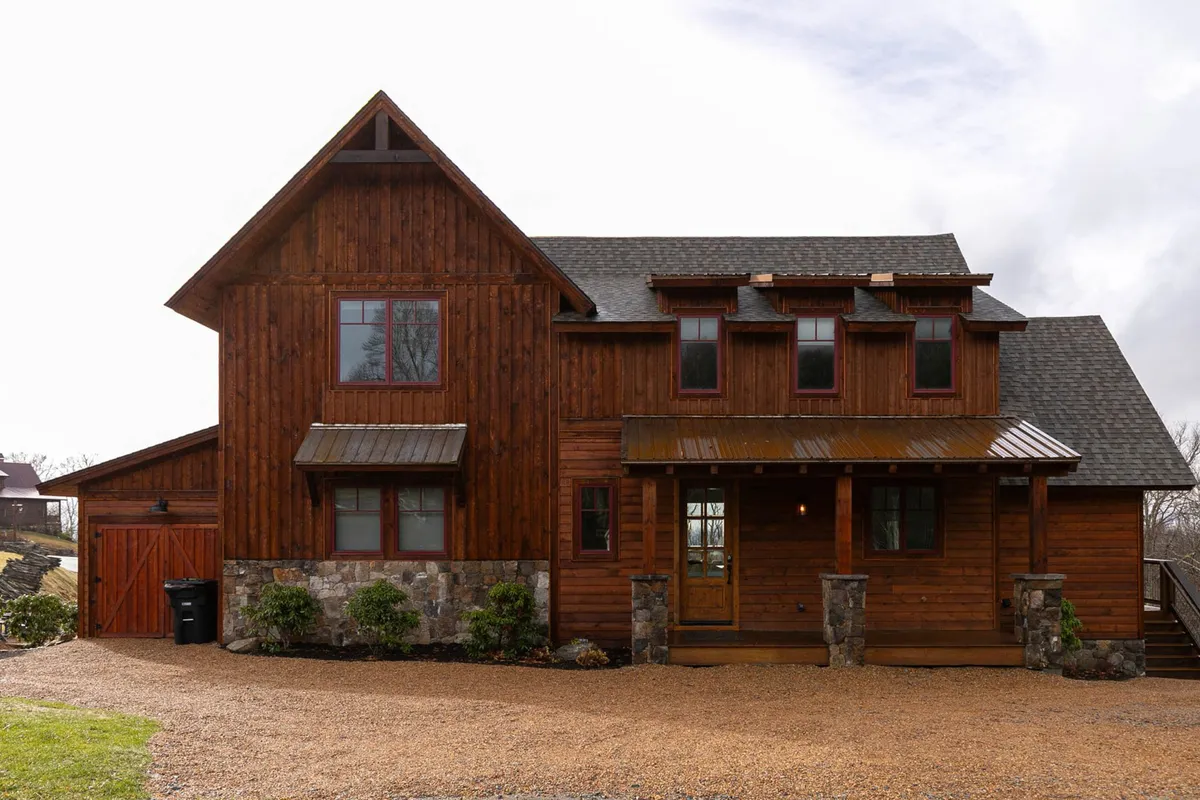An inviting exterior view of Timberline's facade with its wooden and stone accents, a welcoming front porch, and large windows. The yard is set up for gatherings and summer barbecues, emphasizing opportunities for outdoor relaxation and socializing.