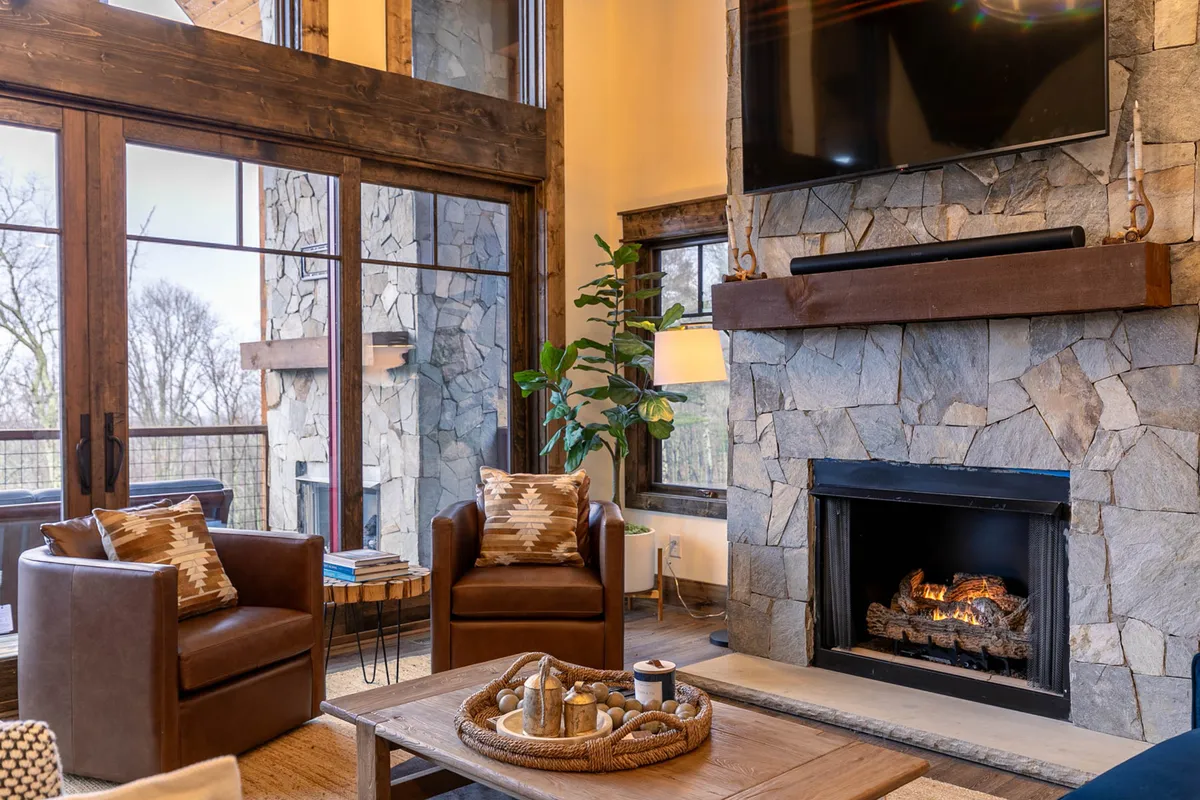 A welcoming indoor space with a stone fireplace, comfortable chairs, a decorative table, and large windows framing the natural landscape. The environment is cozy and ideal for sipping coffee with a view or relaxing after a day outdoors.
