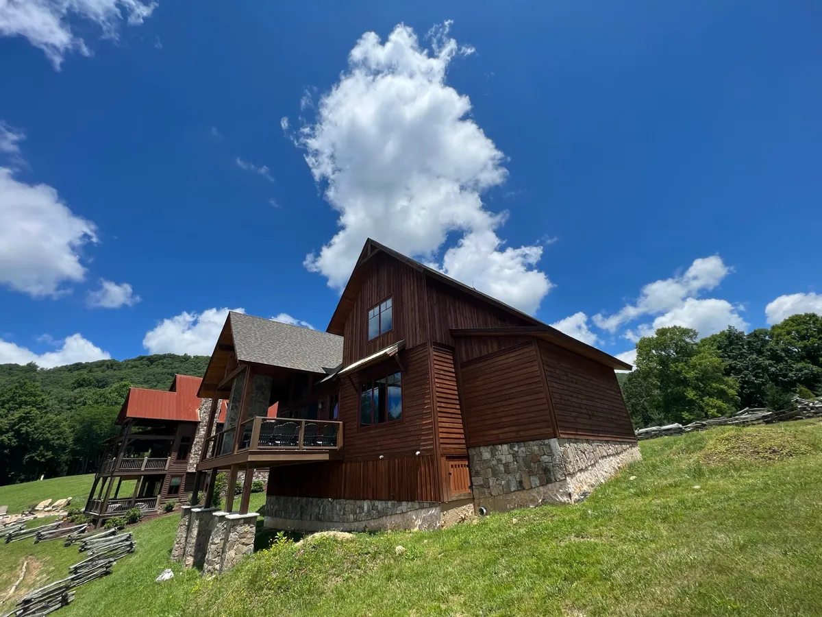 The wooden exterior of the house sits atop a solid stone foundation under an expansive mountain sky. The deck area, visible in the image, is perfect for family gatherings, outdoor relaxation, and appreciating sunset views or stargazing at night.