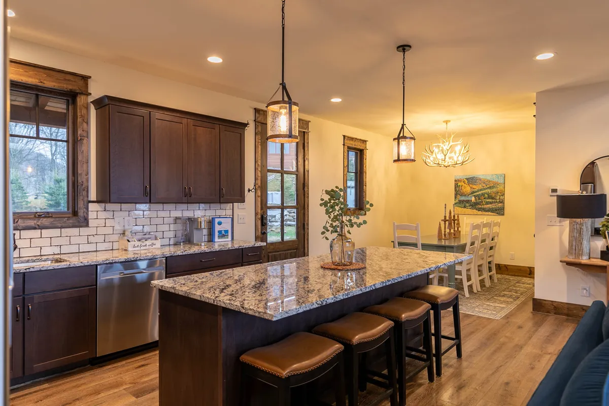 A well-appointed kitchen with a granite island and stools, dining area with a sparkling chandelier, and windows letting in soft daylight. The setting is perfect for casual breakfasts, festive holiday gatherings, or quiet coffee moments.
