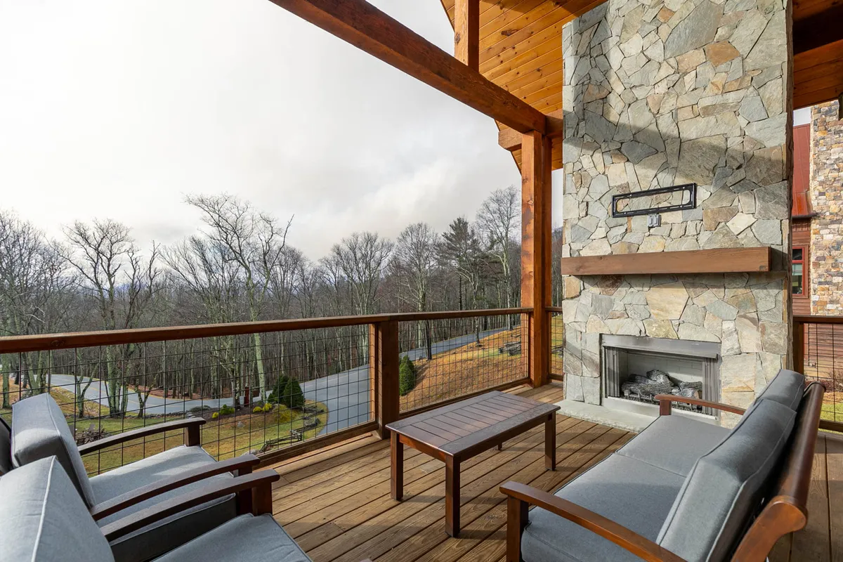 A tranquil wooden deck features an inviting stone fireplace, comfortable outdoor seating, and is set against a stunning scenic mountain view. The space is ideal for relaxing, socializing, or enjoying sunrise coffee and cozy evenings outdoors.