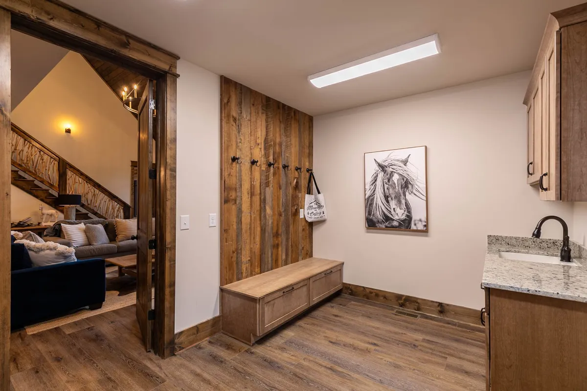 This image captures a welcoming entryway with a wooden bench, horse artwork, and wall hooks. The bench is well-positioned for taking off muddy boots or organizing gear, while the hooks offer practical hanging space for coats, bags, and outdoor essentials. The decor creates a cozy, organized atmosphere right at the home’s threshold.