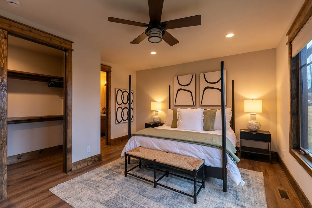 This image shows a tranquil bedroom featuring a four-poster bed with soft linens, decorative wall art, nightstands with lamps, and a bench at the foot of the bed. Natural light filters in, creating a restful and inviting ambiance that encourages relaxation and comfort.